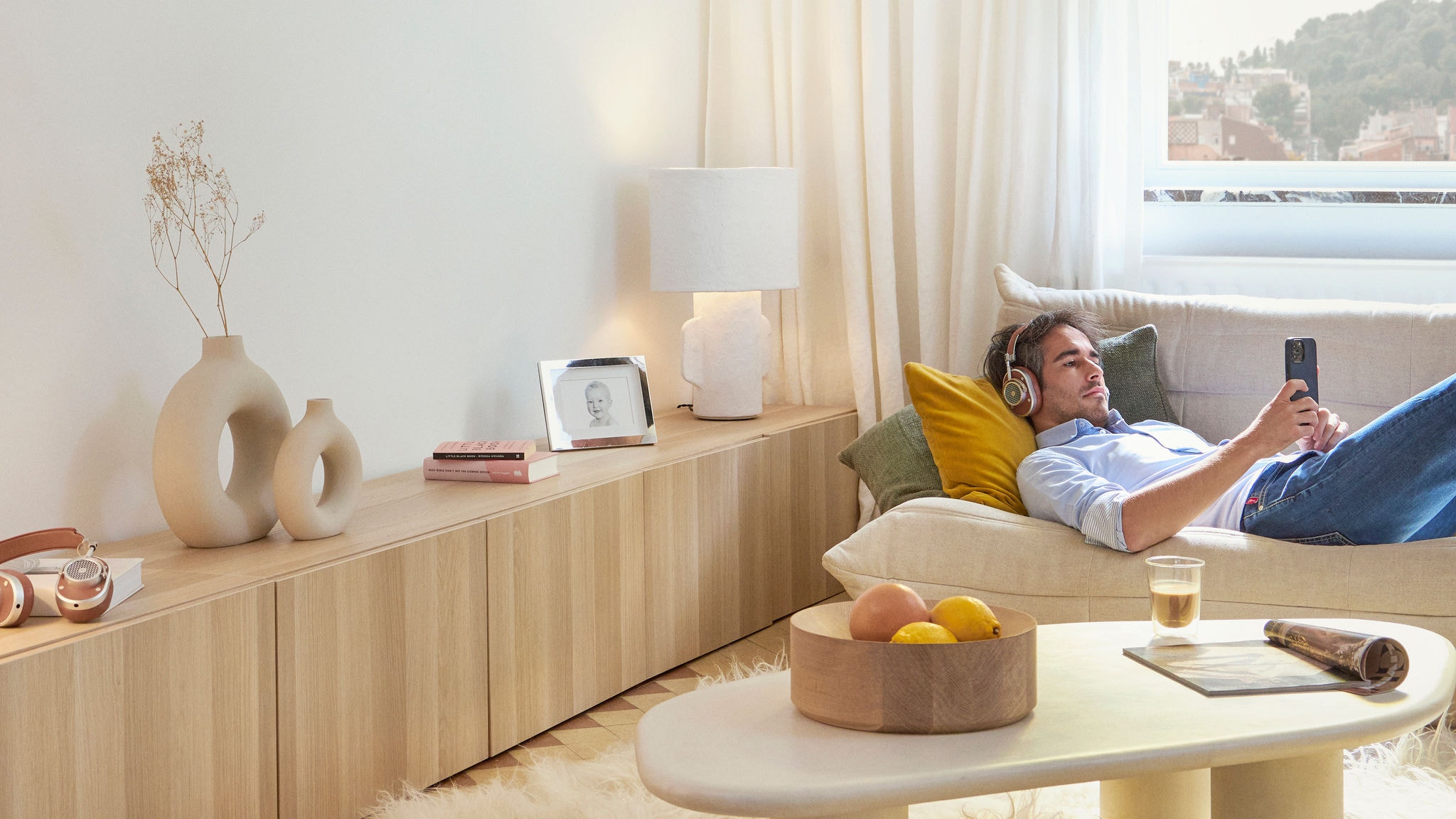Relaxed man lying down on couch with headphones scrolling on phone in living room