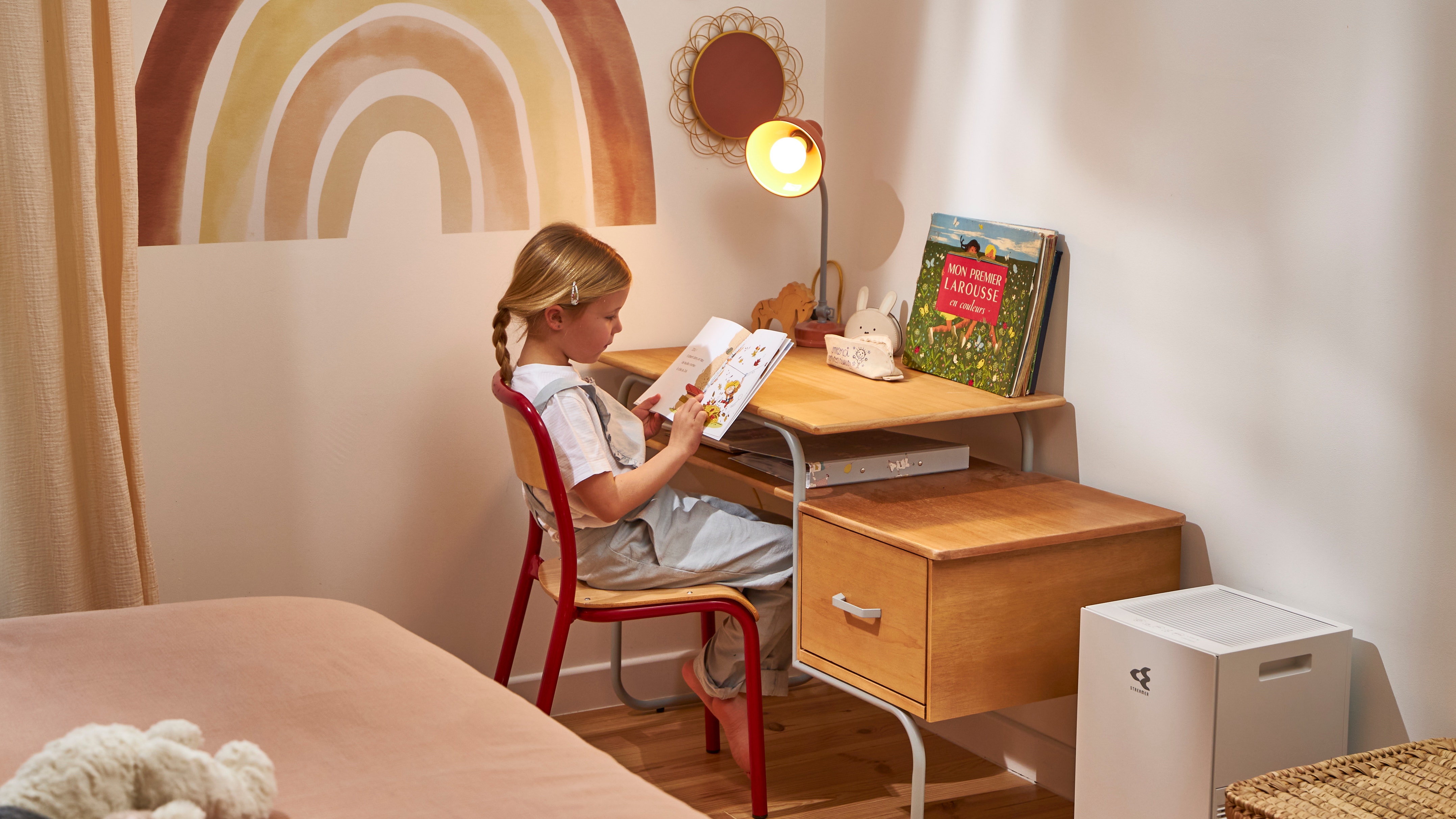 Enfant qui lit un livre tout en respirant un air sain grâce au purificateur d'air placé à côté de son bureau