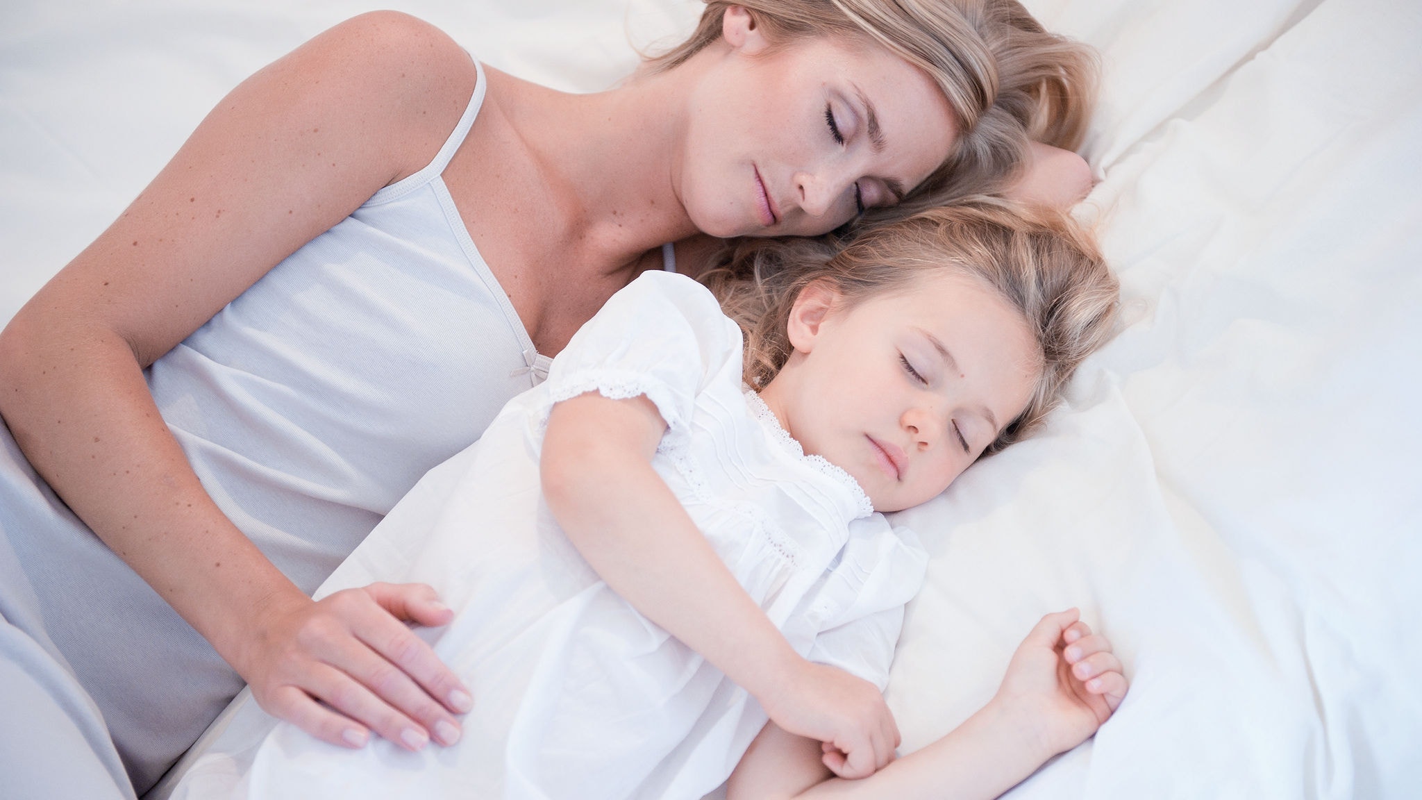 La mère et la fille dormant l'une à côté de l'autre dans un lit blanc et respirant de l'air pur