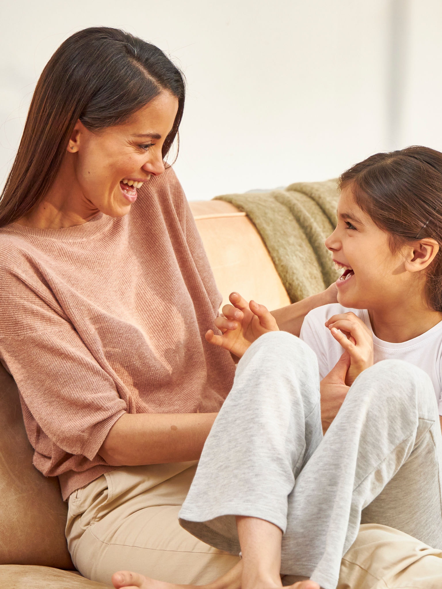 Mother cuddling her daughter while they are both laughing on the couch