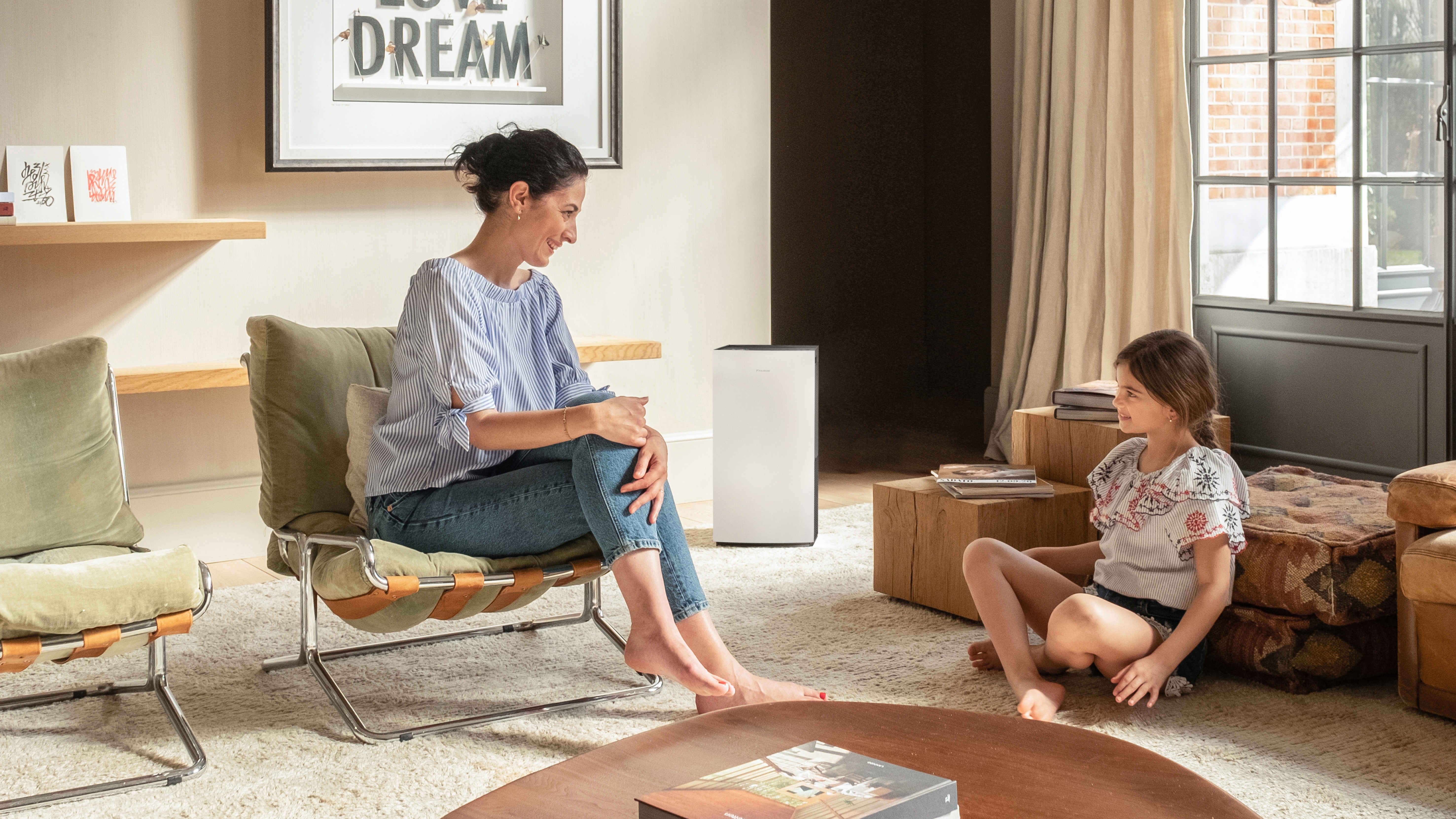Mère parlant joyeusement à sa petite fille dans le salon où l'air est purifié grâce à un purificateur d'air Daikin.