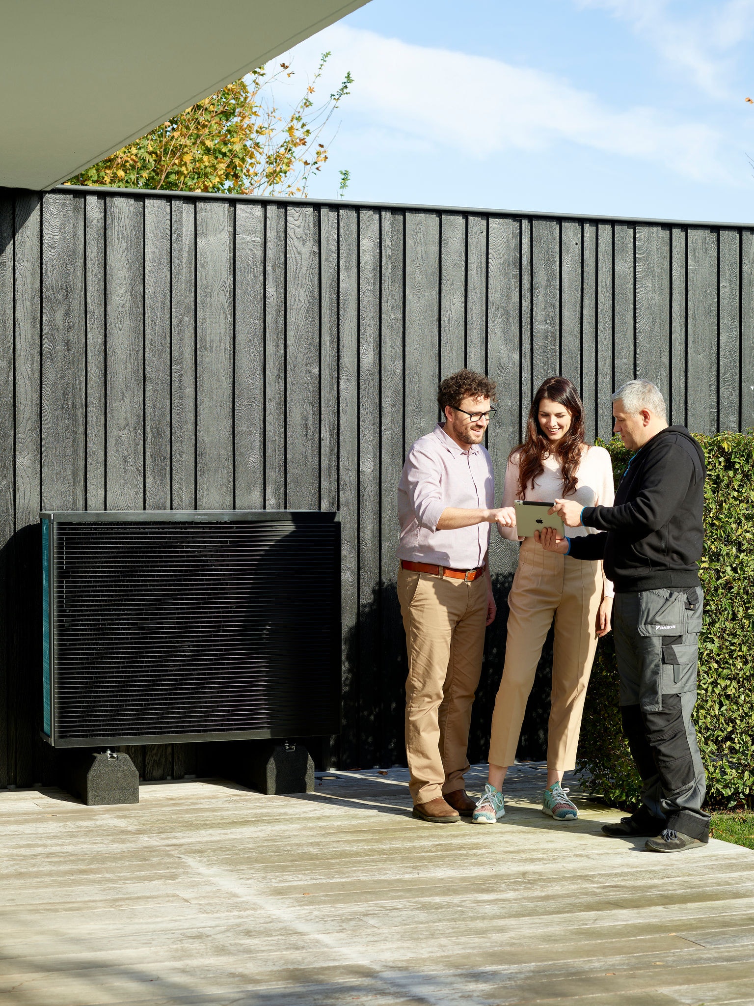 Couple discutant avec l'installateur tout en regardant sur une tablette à côté du groupe extérieur d'un Daikin Altherma